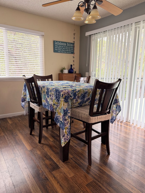 Un comedor con una mesa cubierta con mantel floreado, rodeado de sillas de madera con asientos acolchados.