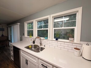 A kitchen with a double sink, white cabinets, and a window with a welcome sign.