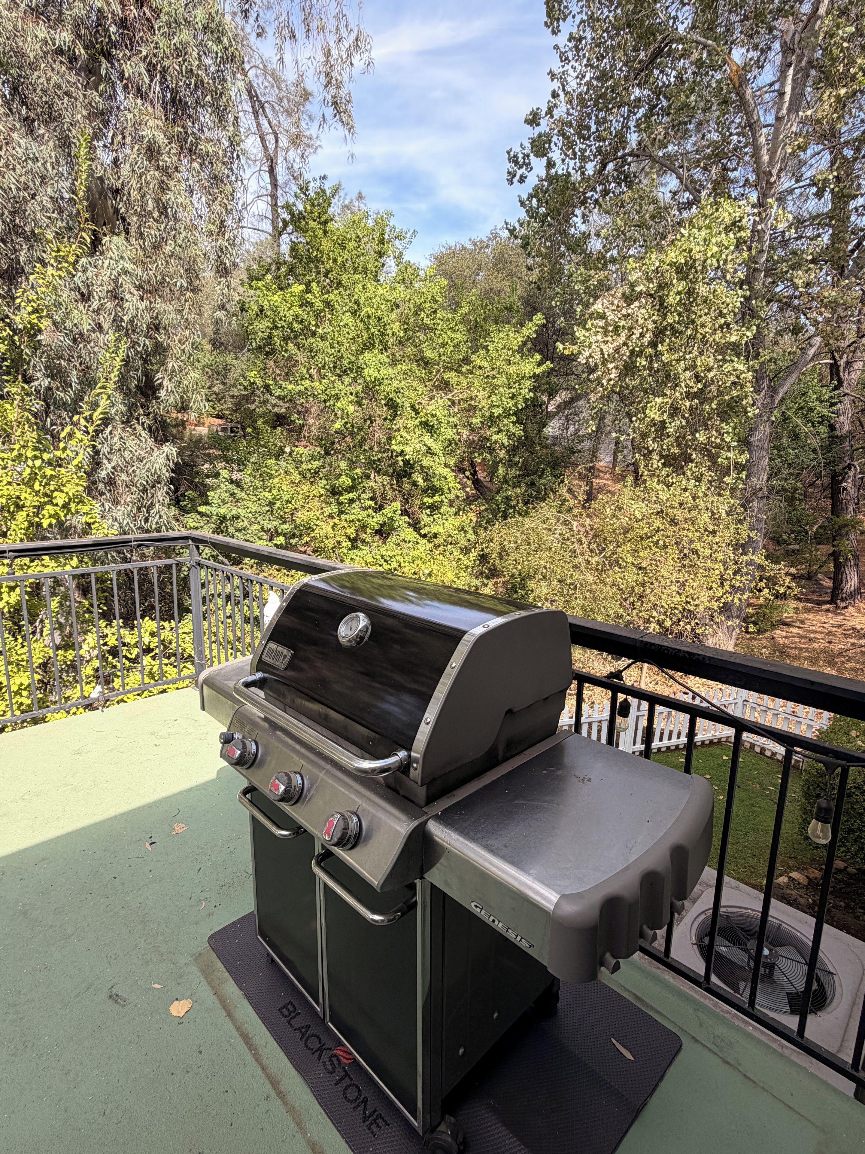 Een draagbare gasgrill met een digitaal display, op een balkon met uitzicht op een bebost gebied.