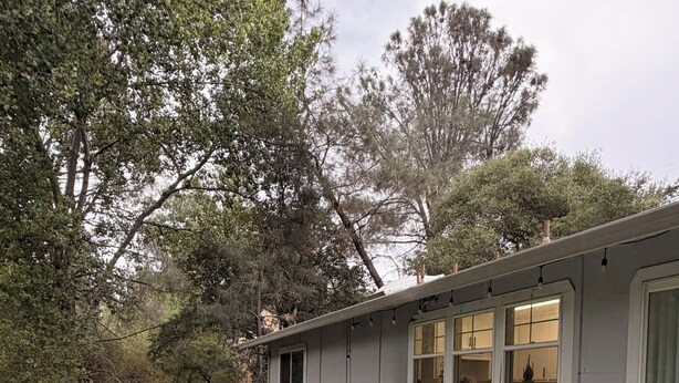 Un patio exterior con una mesa y sillas, una parrilla y vistas a árboles y un edificio.