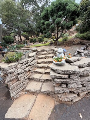 A garden with stone steps leading to a seating area with a decorative bowl and flowers.