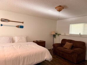 Ein Schlafzimmer mit einem Bett, einem braunen Sofa, einem Nachttisch, einer Lampe und zwei Wanddekorationen in Form von Stand-Up-Paddles.