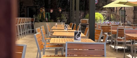 Un espacio al aire libre con mesas y sillas de madera, un ventilador de techo y una pantalla de televisión.