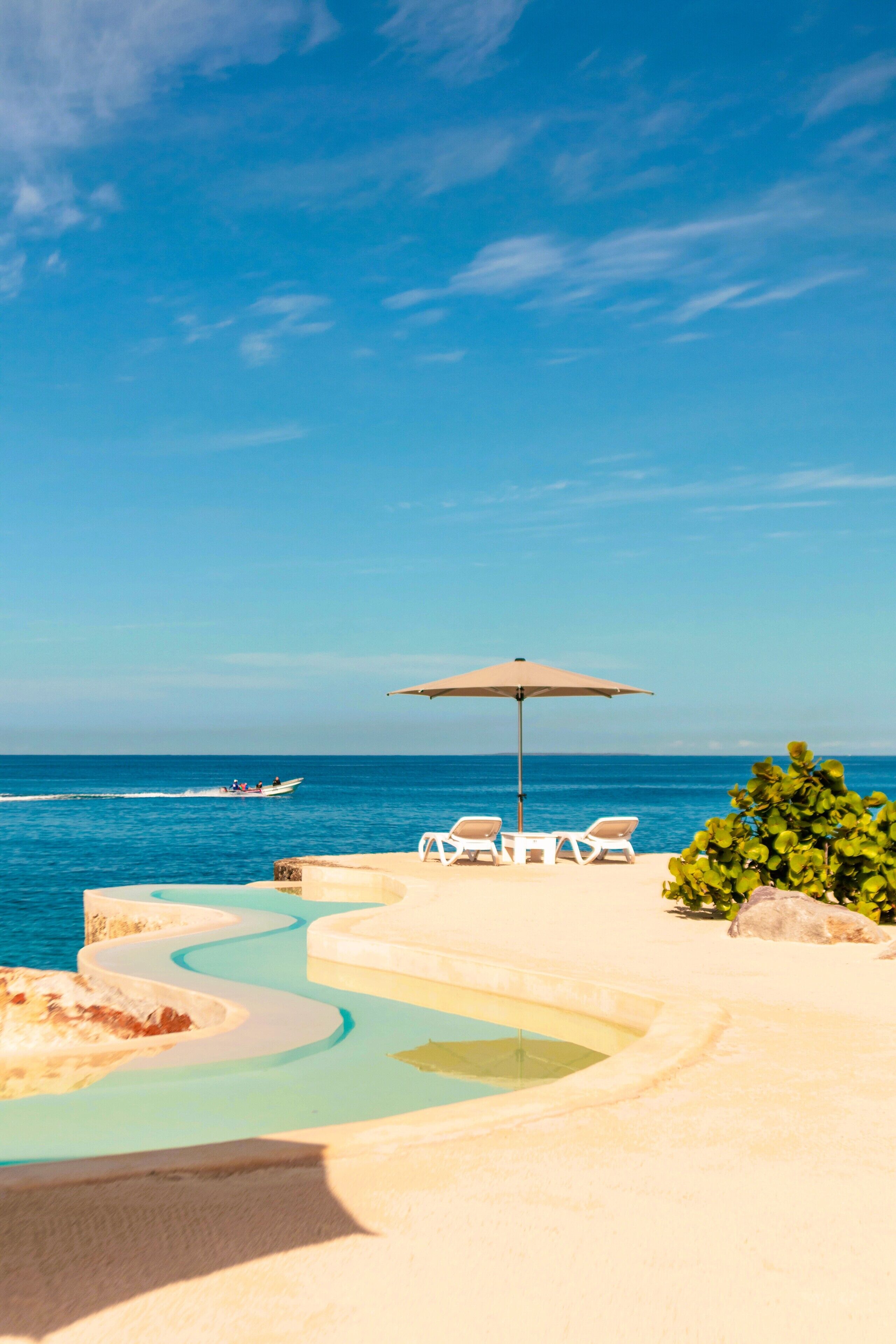 A pool area with lounge chairs and an umbrella, overlooking the sea.