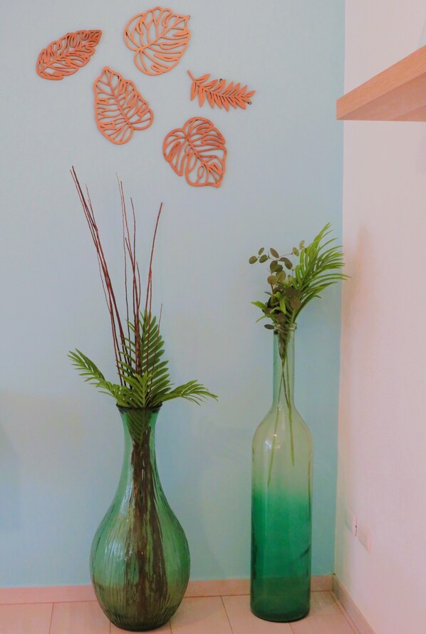 Deux vases ornés de plantes sont posés sur un sol carrelé, devant un mur décoré de motifs de feuilles.