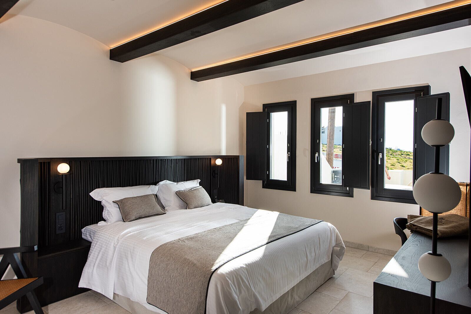 Un dormitorio moderno con una cama grande, una mesita de noche, un escritorio con lámpara y vistas a través de la ventana.