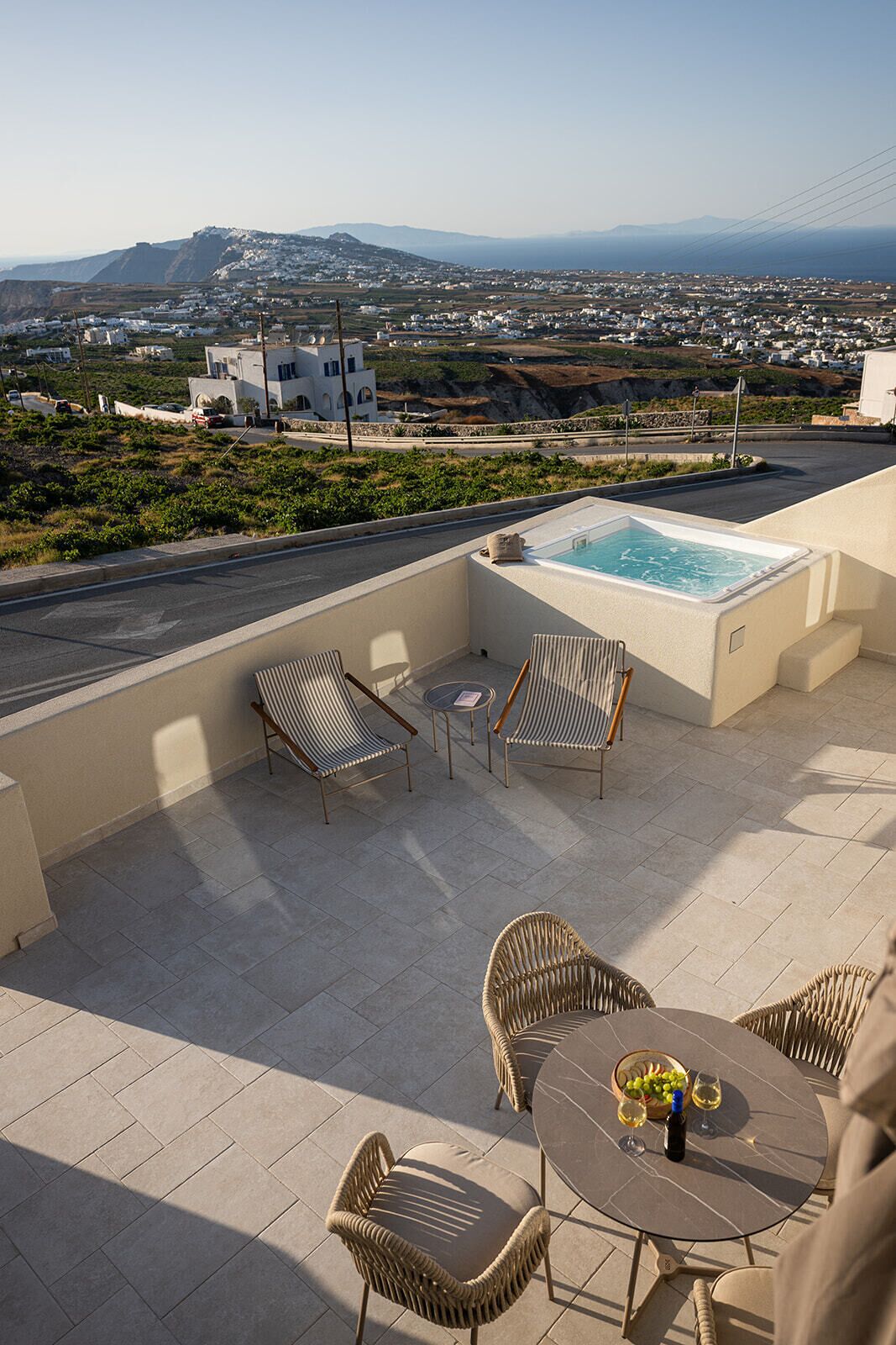 A rooftop terrace with a hot tub, wicker furniture, and a table with a bottle and glass.