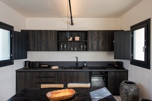 A modern kitchen with dark wood cabinetry, a black countertop, and a built-in oven. - Avento Luxury Suites (Santorini)