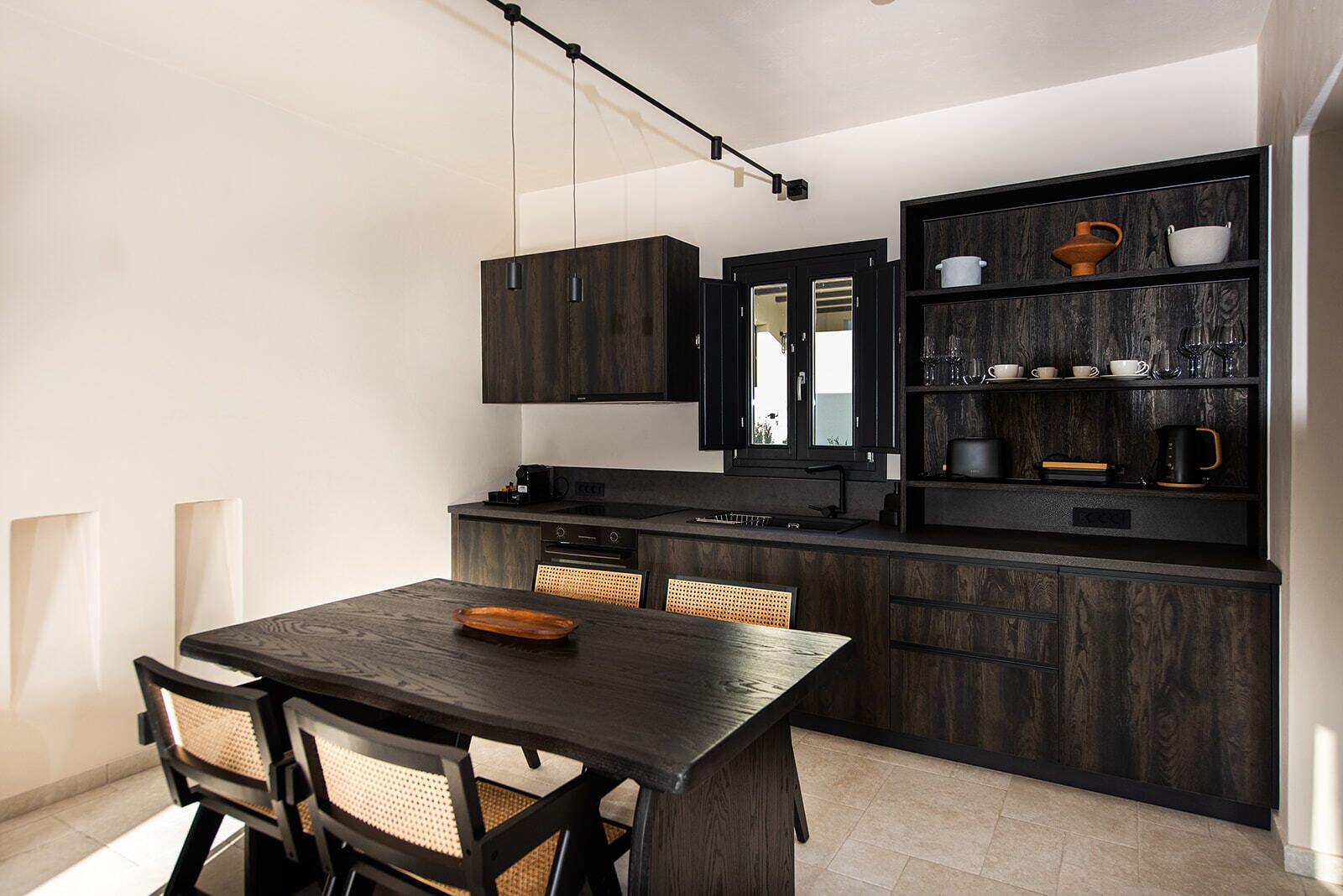 Una cocina moderna con muebles oscuros de madera, horno empotrado y una zona de comedor con mesa y sillas de madera oscura.