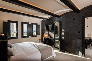Ein modernes Schlafzimmer mit einem großen Bett, einer Wand aus Naturstein und einem Fernseher über einem Schminktisch.