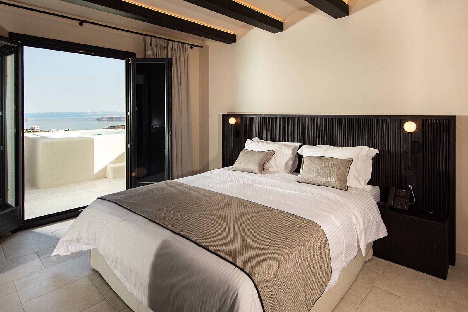 A hotel room with a bed, a nightstand, a telephone, and a view of the sea through a sliding door.