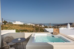 Eine Dachterrasse mit Whirlpool, einem Tisch mit einem Glas und Blick auf eine Küstenstadt.