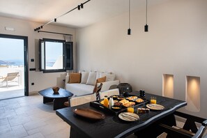 A modern dining area with a breakfast buffet, a sofa, and a view of the outdoors. - Avento Luxury Suites (Santorini)