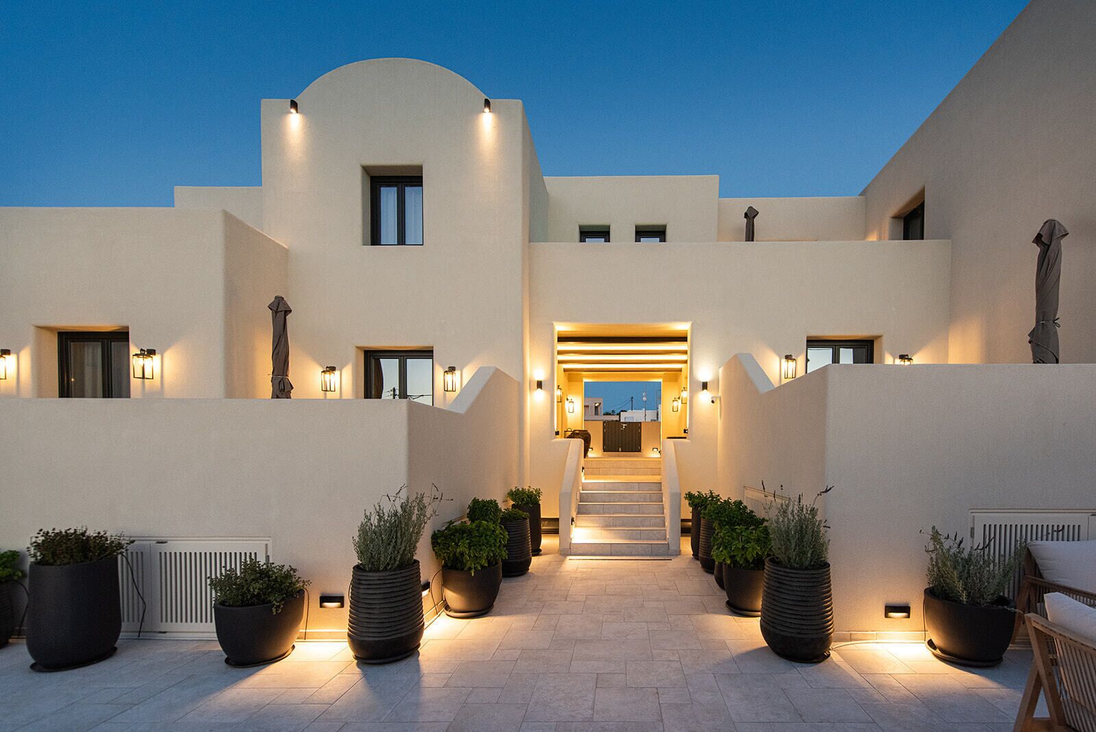 A modern building with a central staircase, potted plants, and exterior lighting.