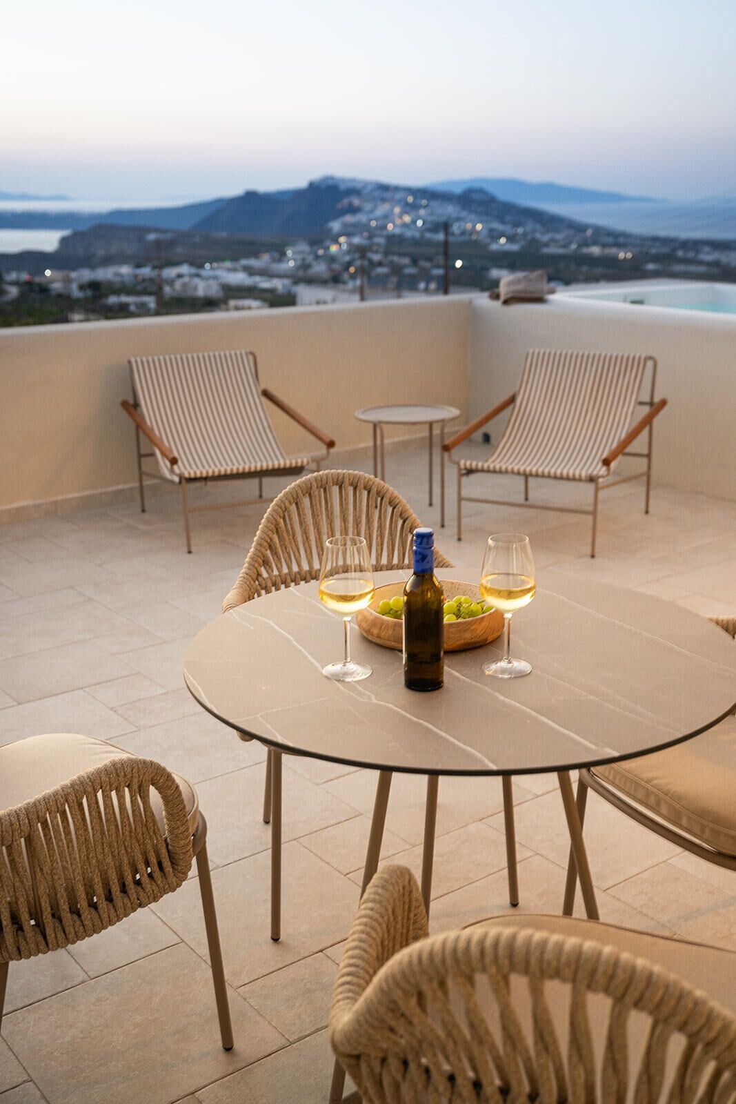 Una terraza con sillones de mimbre, una mesa redonda y una botella de vino.
