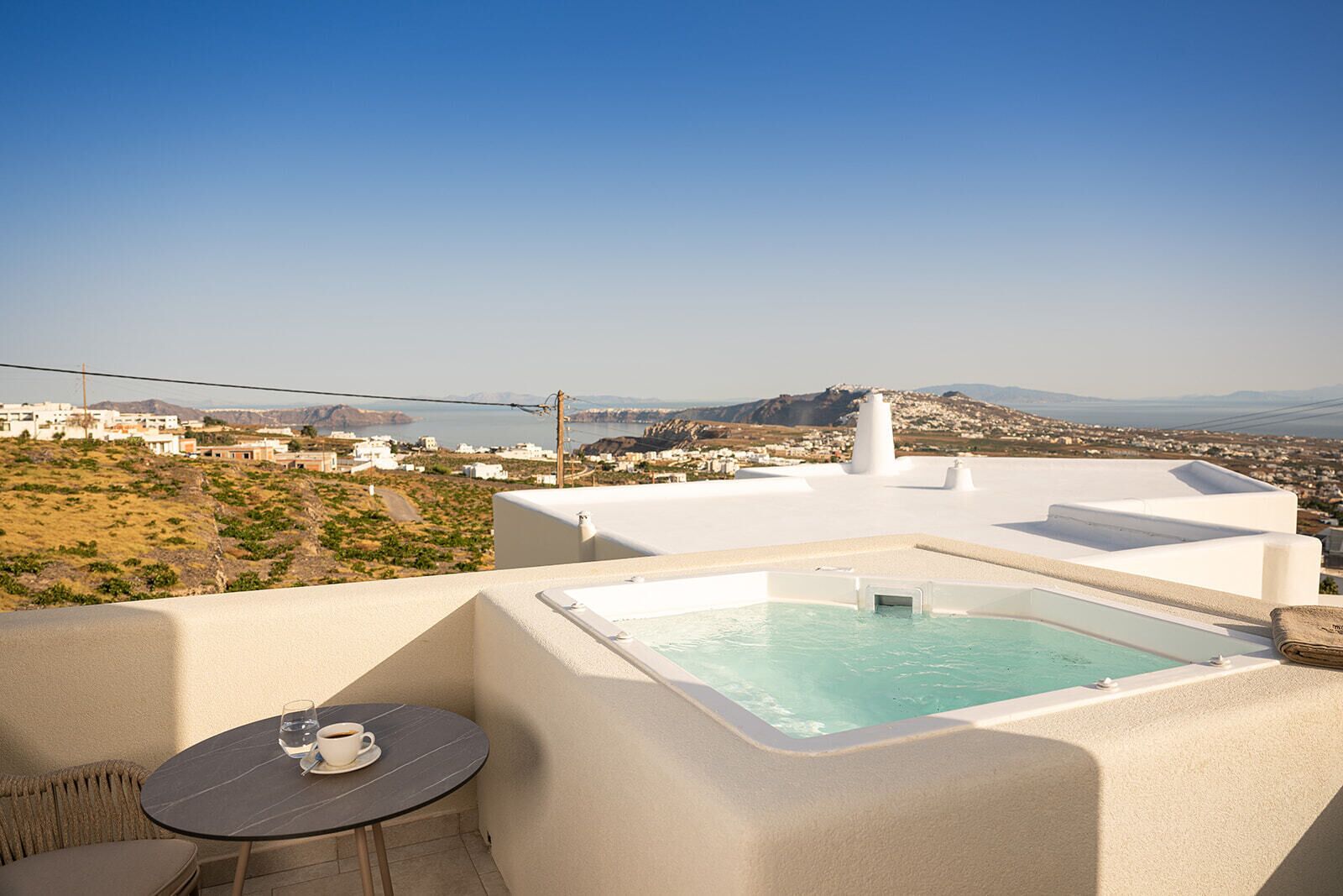 Eine Dachterrasse mit Whirlpool, einem Tisch mit einer Tasse und Blick auf eine Küstenstadt.
