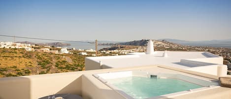 A rooftop terrace with a hot tub, a table with a cup, and a view of a coastal town.