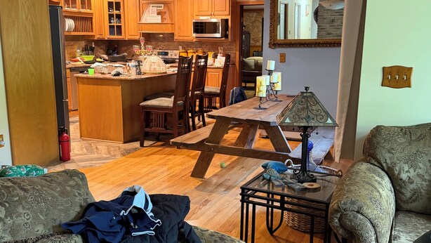 Una sala de estar acogedora con un sofá, una mesa de centro y una lámpara. Se ve una cocina con armarios de madera y un comedor con sillas al fondo.