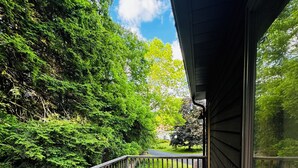 Una terraza de madera con mobiliario de mimbre y un ventanal que da a un paisaje verde exuberante.