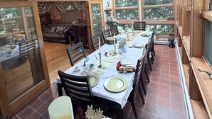 Comedor con una mesa dispuesta para seis personas, ventanas amplias y vistas al exterior con vegetación.