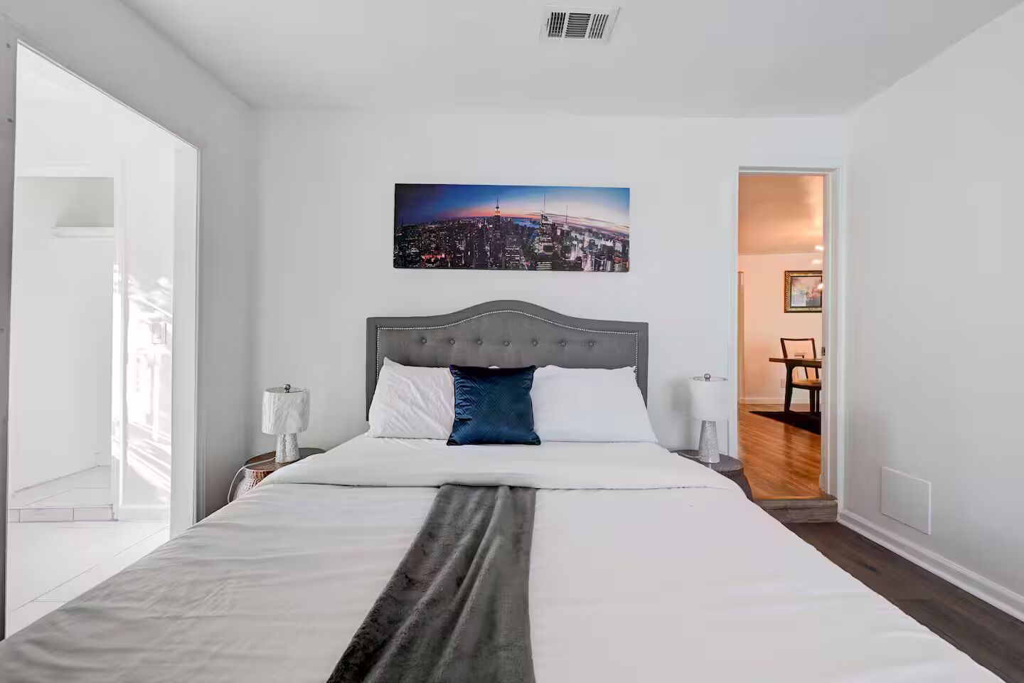Ein Hotelzimmer mit einem großen Bett, einem Stadtbildgemälde und Blick auf die Stadt durch das Fenster.