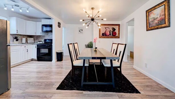 A modern kitchen with white cabinets, a black stove, and a dining area with a wooden table and chairs. - Homey & Spacious 4-bedroom house in fabulous Austin neighborhood (Austin)