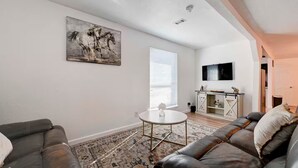 A living room with a sofa, a coffee table, a painting, a TV, and a sliding door leading to another room. - Homey & Spacious 4-bedroom house in fabulous Austin neighborhood (Austin)