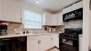 A kitchen with white cabinets, a black stove, a dishwasher, and a window with blinds. - Homey & Spacious 4-bedroom house in fabulous Austin neighborhood (Austin)