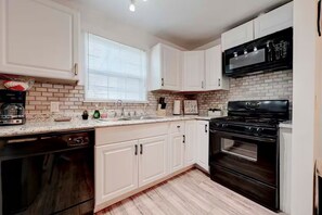 A kitchen with white cabinets, a black stove, a dishwasher, and a window with blinds. - Homey & Spacious 4-bedroom house in fabulous Austin neighborhood (Austin)