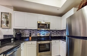 A kitchen with white cabinets, a stainless steel refrigerator, a microwave, and a stove. - Tidewater 1800 (Panama City Beach)