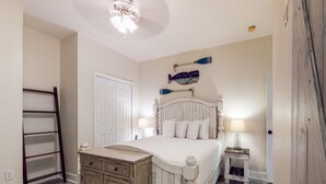 Um quarto com uma cama, cômoda, escada, porta e uma luminária fixada na parede.