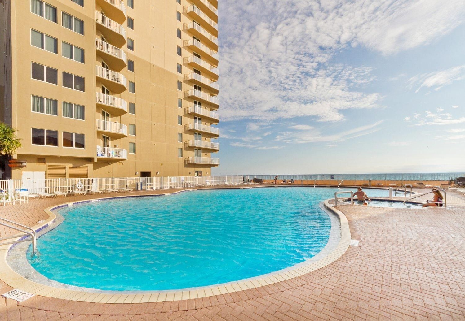 Una piscina con vistas claras al océano, rodeada por un edificio de varios pisos con balcones.