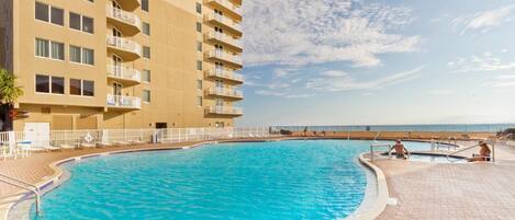 Una piscina con vistas claras al océano, rodeada por un edificio de varios pisos con balcones.