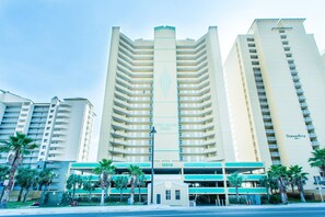Een meerhoog hotel met een centraal verticaal element, een parkeergarage en palmbomen op de voorgrond.