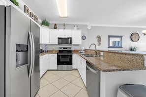 Eine moderne Küche mit weißen Schränken, Edelstahlgeräten, einer Granitabdeckung und einem gefliesten Boden.