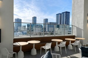 A rooftop terrace with round tables and white chairs, overlooking a cityscape with high-rise buildings. - Comfy Condo-Hotel in Downtown Miami (Miami)