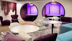 Un área de descanso moderna con mesas redondas, sillas moradas y blancas, y un diseño de pared circular único.