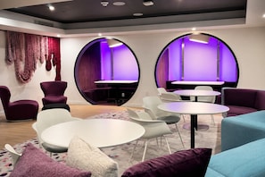 A modern lounge area with round tables, purple and white chairs, and a unique circular wall design. - Comfy Condo-Hotel in Downtown Miami (Miami)