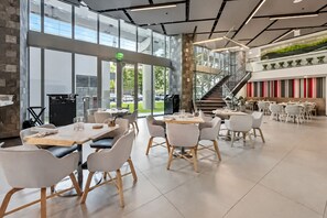 A modern dining area with multiple tables and chairs, a staircase, and a view of the outdoors. - Comfy Condo-Hotel in Downtown Miami (Miami)