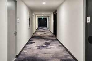 Een hotelgangen met vloerbedekking, deuren aan beide kanten en een bordje met de aanduiding van de uitgang.