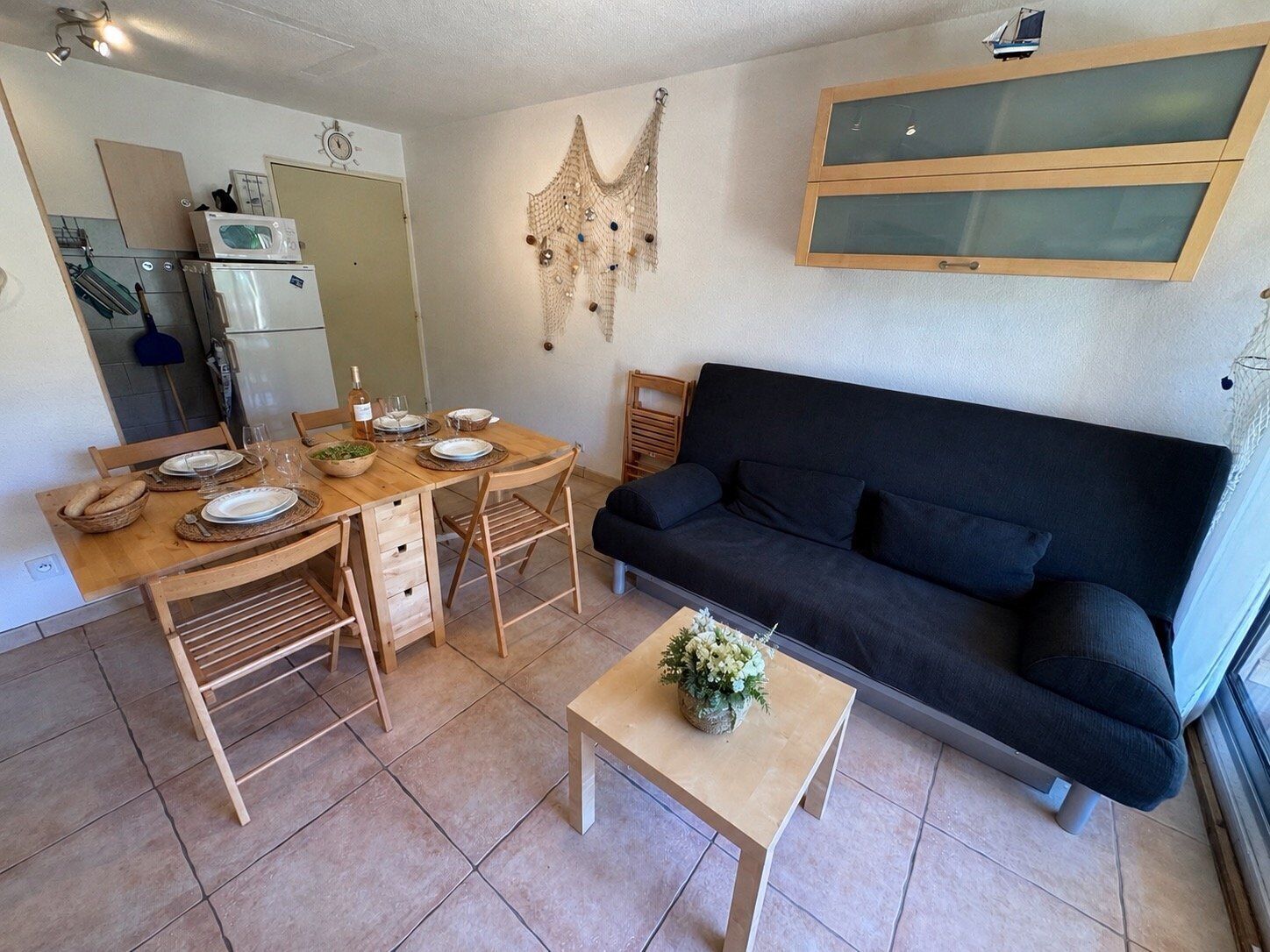 Un espace de vie compact comprenant une table à manger, des chaises, un canapé, une petite table basse et un coin cuisine équipé d’appareils électroménagers.