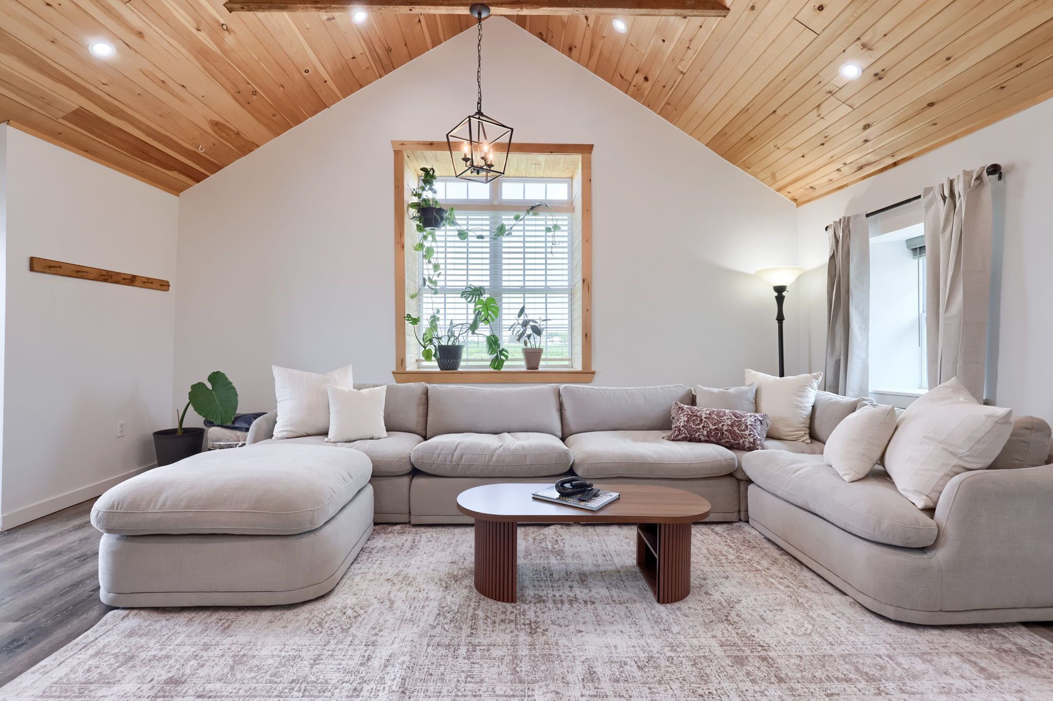 Un salon moderne avec un canapé d’angle, une table basse et une grande fenêtre agrémentée de plantes.