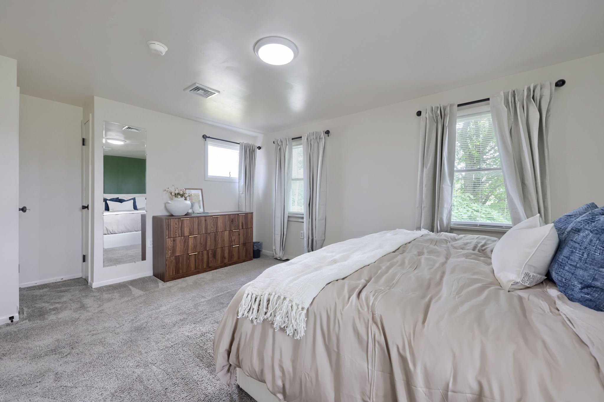 Een slaapkamer met een bed, een dressoir, een raam met gordijnen en een deur naar een andere kamer.