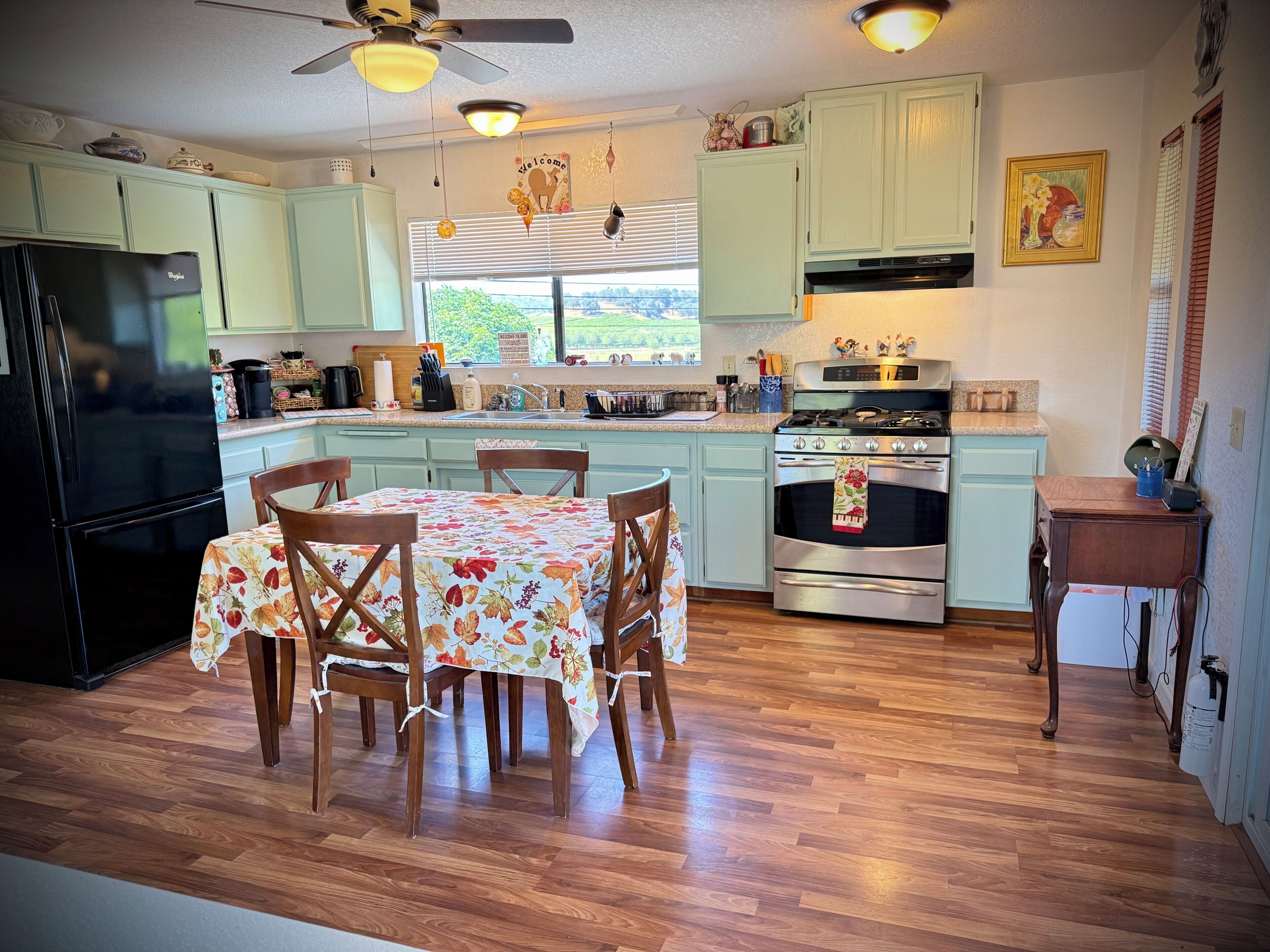 A kitchen with a dining table, chairs, a refrigerator, stove, and a window with blinds.