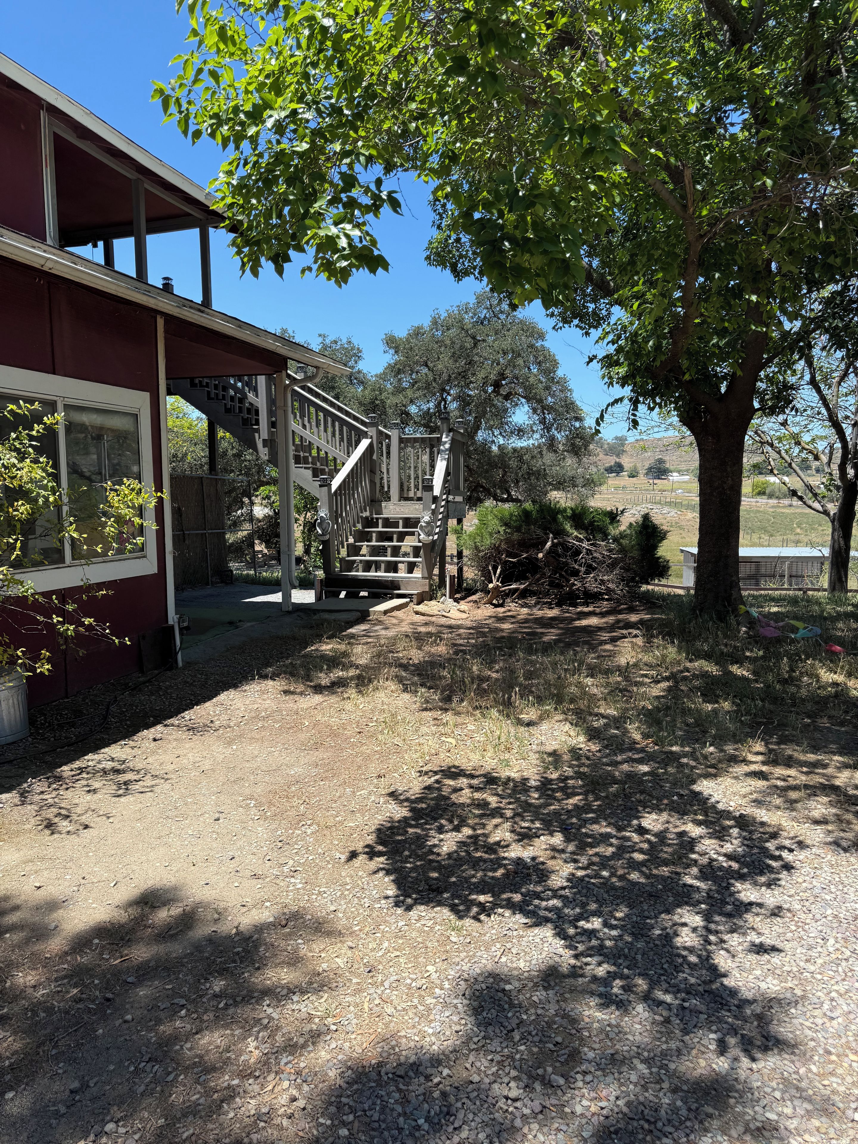 A building with a covered porch, a staircase leading to a deck, and a tree in the foreground.