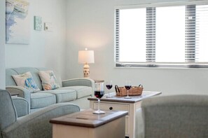 Ein Wohnzimmer mit einer Couch, einem Couchtisch mit Weingläsern, einer Lampe und einem Fenster mit Jalousien.
