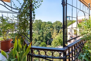 A balcony with a metal railing overlooking a dense green forest and a cityscape. - Spazio Santana (Milano)