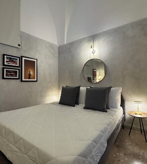 A bedroom with a bed, pillows, a round mirror, a small table with a lamp, and framed pictures on the wall. - Cozy oceanfront apartment with a garden and patio. (Santa Cesarea Terme)