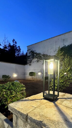 A stone bench with a modern, illuminated lantern in front of a white wall with climbing plants. - Cozy oceanfront apartment with a garden and patio. (Santa Cesarea Terme)