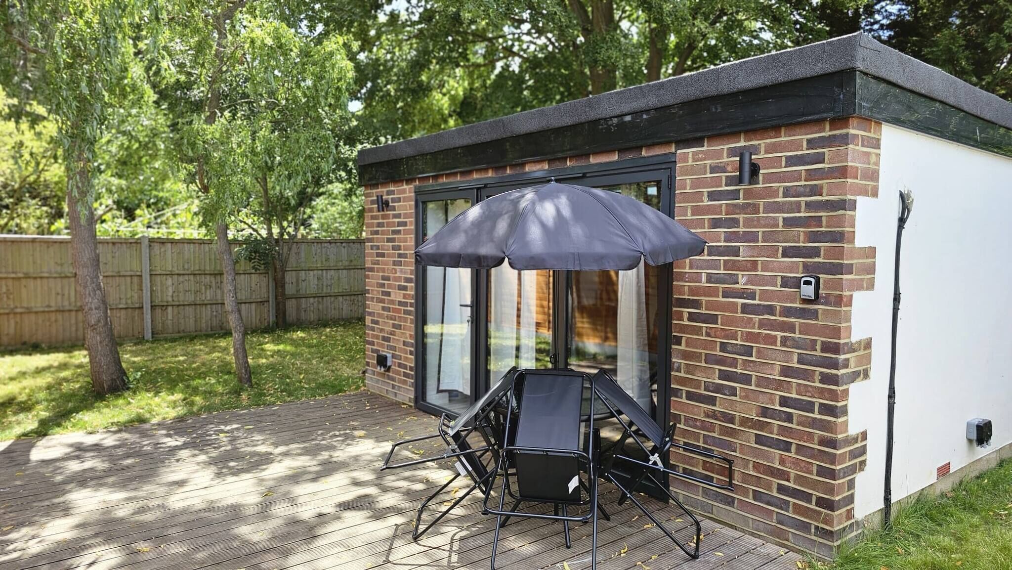 A patio with a table and chairs, a black umbrella, and a brick building with glass doors.